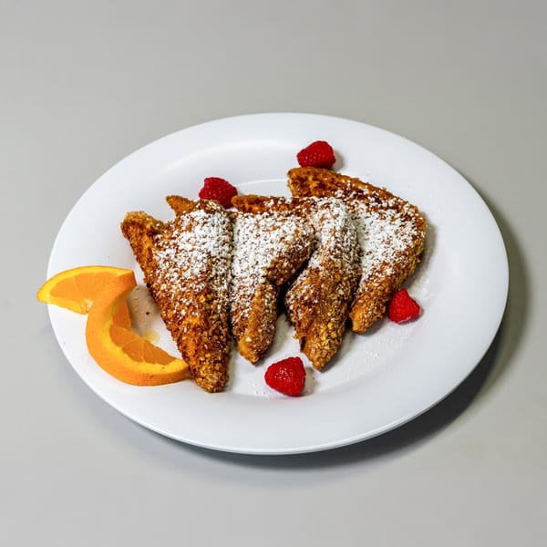 Four pieces of French toast, dusted with powdered sugar, garnished with raspberries and orange slices.