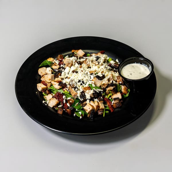 Chicken salad with feta, sun-dried tomatoes, and mushrooms, served with a side of dressing.