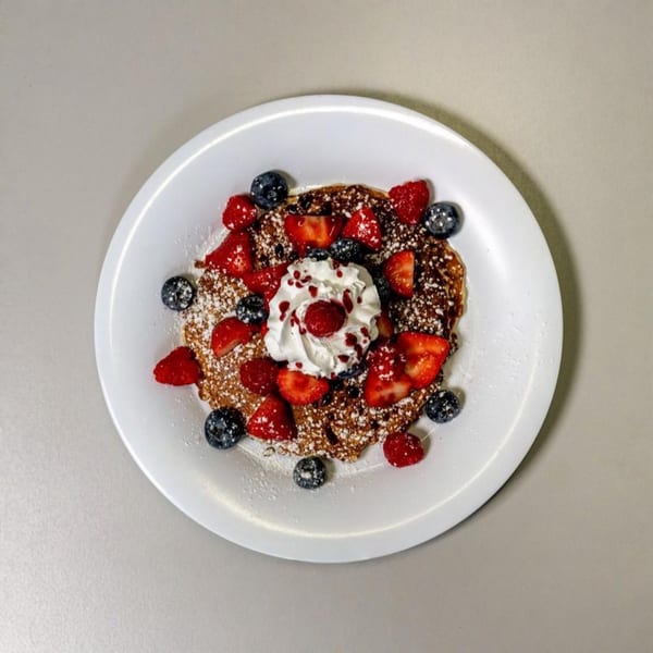 A waffle topped with whipped cream, strawberries, blueberries, raspberries, and powdered sugar.